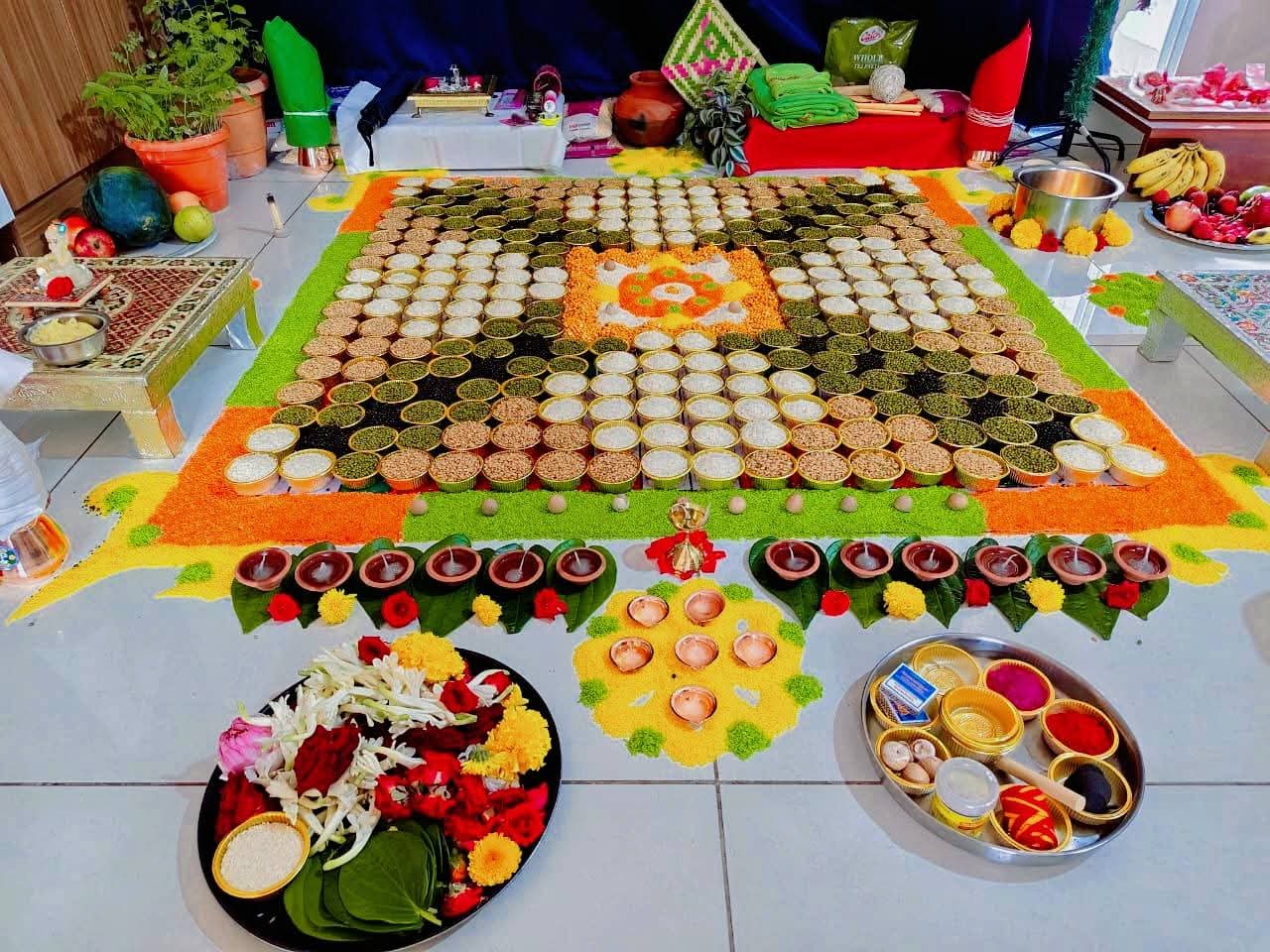 A grain mandala laid on the floor for a home puja, with lamps and flower offerings
